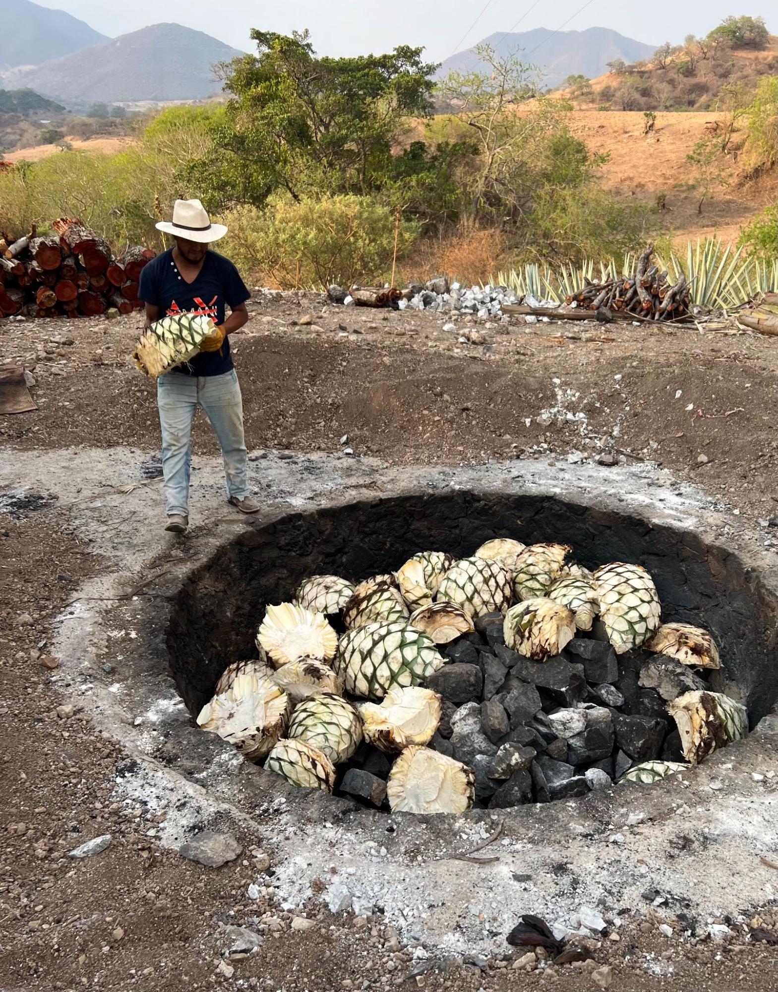 Mezcalero loading agave piñas into the conical volcanic-rock oven at Mezcal Argato
